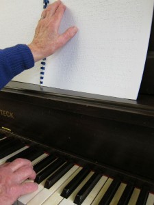 one hand on braille music and another hand on a piano keyboard