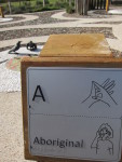 Sign in playground for the letter a with braille, finger spelling and Auslan for the word "aboriginal"